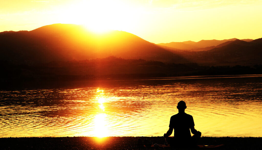 Silhouette of a man meditating on a lakeshore